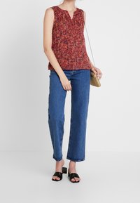 Top senza maniche floreale rosso e multicolore con scollatura a V, abbinato a jeans blu a vita alta e sandali neri con tacco a blocco.