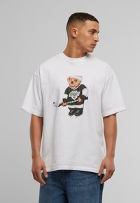 White short-sleeve t-shirt featuring a cartoon bear in hockey gear, holding a stick. Crew neck, relaxed fit, cotton material.