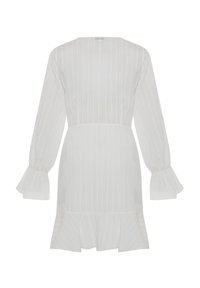 Robe blanche à manches longues avec des rayures verticales, poignets évasés, taille cintrée et ourlet à volants, vue de dos.