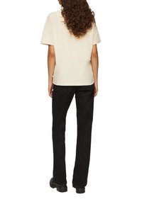 Beige katoenen T-shirt met korte mouwen, rechte snit en een ronde halslijn, gecombineerd met zwarte rechte broek en zwarte laarzen.