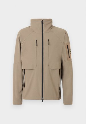 Μπεζ μπουφάν με ψηλό γιακά, εμπρόσθιο μαύρο φερμουάρ, δύο κάθετες τσέπες με φερμουάρ στο στήθος, τσέπες με φερμουάρ στα πλάγια και τσέπη με φερμουάρ στο αριστερό μανίκι.