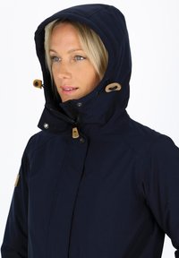 Ciemnoniebieska wodoodporna kurtka z kapturem wyłożonym futerkiem, regulowanymi sznurkami i drewnianymi akcentami na zapięciach. Posiada zamek błyskawiczny i zatrzaskowe zapięcie.