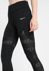 Czarne legginsy z wysokim stanem, z siateczkowymi wstawkami i wzorami tekstowymi "NIKE". Wykonane z elastycznego, fakturowanego materiału dla komfortu.