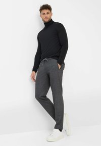 Zwarte coltrui gecombineerd met grijze broek met koord, beide gemaakt van een gestructureerde stof. Model draagt witte sneakers. Eenvoudige en casual uitstraling.