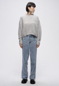 Hellgrauer Strickpullover mit weiten Ärmeln und geripptem Rundhalsausschnitt, kombiniert mit hellblauen, hoch taillierten Jeans. Das Modell trägt schwarze Plateau-Stiefel.