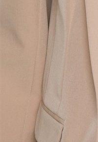 Beige fabric with a smooth texture; features a side pocket and clean stitching. Subtle color variations enhance the design.