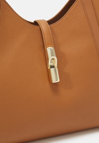 Barna bőrtáska vállra, sima textúrával, arany színű záróelemmel és elegáns, lekerekített formával.