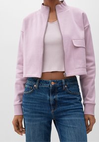 Giacca corta con zip in cotone rosa chiaro, dotata di colletto rialzato e tasca frontale, abbinata a jeans in denim blu a vita alta.