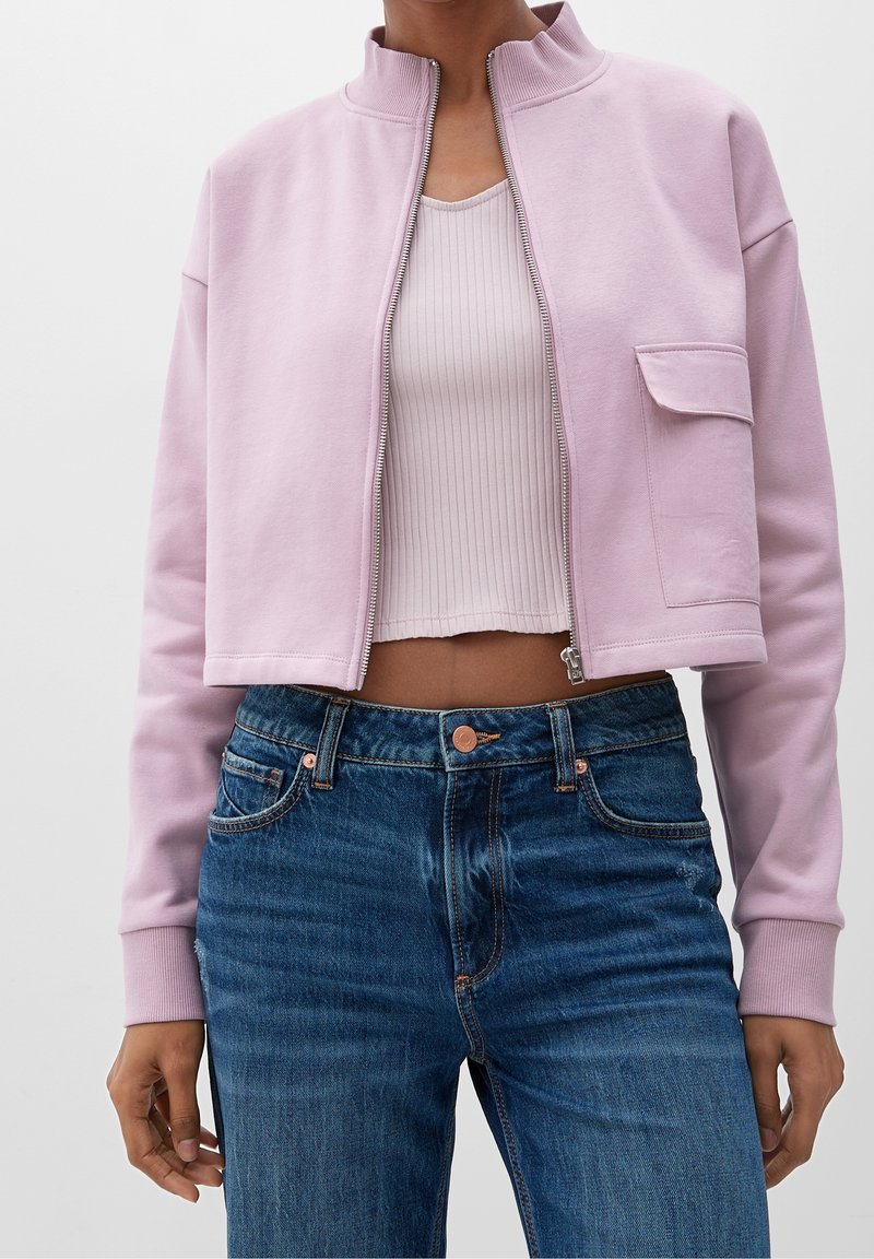 Giacca corta con zip in cotone rosa chiaro, dotata di colletto rialzato e tasca frontale, abbinata a jeans in denim blu a vita alta.