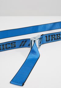 Mėlynas poliesterio diržas su juodu kraštu, su metaliniu užtrauktuku ir logotipo užrašu, skirtas daiktams pritvirtinti arba užfiksuoti.