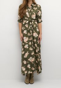 Robes maxi en tissu vert olive avec des motifs floraux en rose et bleu. Elle présente un devant à boutons, un col, une taille cintrée et des manches évasées.