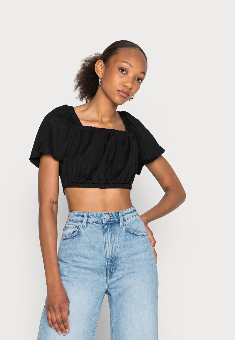 Top preto cropped com bainha elástica, decote quadrado e mangas curtas bufantes, combinado com jeans de ganga de cintura alta em azul claro.