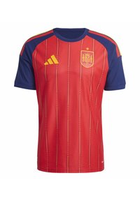 Maglietta rossa a maniche corte con spalle blu, decorata con righe gialle e uno stemma. Realizzata in tessuto leggero con motivi testurizzati.