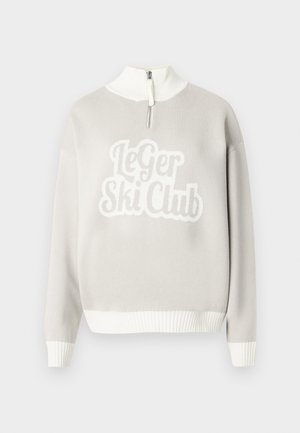 Lys grå genser med hvit ribbestrikket kant og krage, med et tydelig teksturert design "Le Ger Ski Club" på forsiden. Glidelås halvt åpnet.