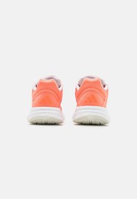 Baskets de sport corail avec une semelle blanche rembourrée. L'arrière présente un logo et une texture lisse, conçus pour le confort et le soutien.