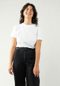 T-shirt en coton blanc à manches courtes, encolure ronde ; associé à un pantalon noir taille haute avec fermeture à bouton et texture subtile.