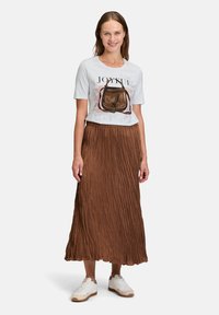 Hvid t-shirt med grafisk print der står "JOYFUL," parret med en brun plisseret nederdel. Modellen bærer hvide sneakers. Enkel, afslappet påklædning.