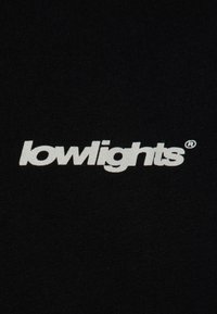 Černá látka s textem "lowlights" v tučném bílém písmu. Materiál vypadá hladce a má konzistentní texturu.