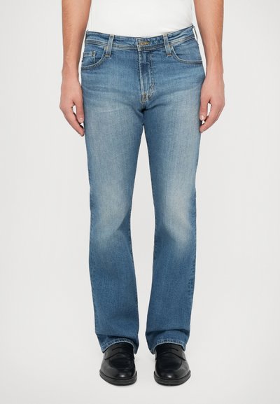 Men's blue denim jeans, straight cut with faded sections, five pockets, belt loops, and sturdy stitching. Worn with black leather shoes.