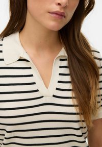 Stripet strik polo i creme og sort med V-udskæring og korte ærmer, med blød tekstur og et klassisk mønster.