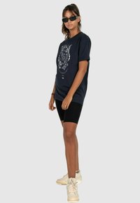 Mørkeblå bomulds t-shirt med hvid grafisk design, parret med sorte cykelshorts og lyse sneakers. Accentueret med sorte solbriller.
