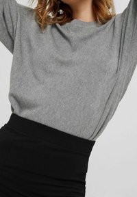 Pull en maille grise avec un col rond et des manches longues, associé à une jupe noire taille haute. Texture douce et coupe décontractée.