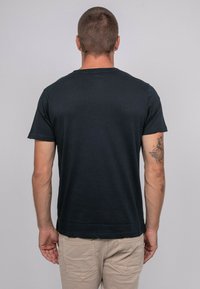 T-shirt en coton noir à manches courtes et col rond. Texture lisse, design simple, sans graphiques ni motifs visibles.