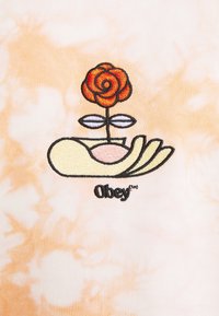 Une main stylisée tenant une rose rouge avec deux feuilles blanches sur un fond tie-dye orange clair, avec le mot "Obey" en dessous.