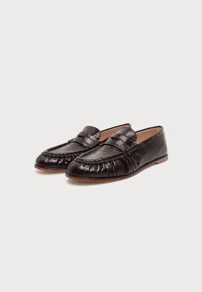 Paire de mocassins en cuir marron foncé avec un motif façon crocodile et des semelles basses en bois, positionnés côte à côte sur un fond uni.