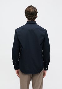 Chemise bleu marine à manches longues en coton, dotée d'un col classique, de poignets à boutons et d'un ourlet arrondi, vue de dos.