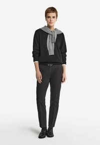 Svart tröja med en grå scarf knuten vid halsen, tillsammans med slim-fit svarta byxor och svarta skor. Mjuka texturer, avslappnad design.