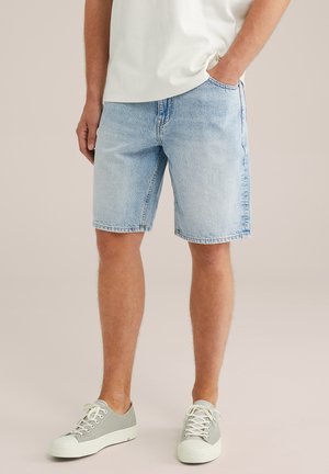 Shorts din denim de culoare albastru deschis, cu croială dreaptă, cinci buzunare și cusături vizibile. purtați cu adidași gri și un tricou alb simplu.