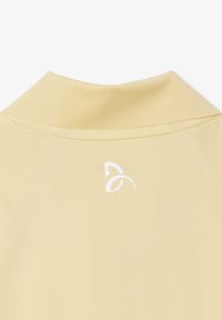 Indumento beige a collo alto con un logo stilizzato di foglia bianca centrato sotto il colletto sul retro.