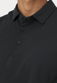 Schwarzes Poloshirt mit strukturiertem Kragen, versehen mit drei passenden Knöpfen und einem glatten, strukturierten Stoff. Keine sichtbaren Logos oder Muster.