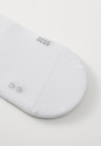Calcetín de algodón blanco con una textura suave. Los detalles incluyen "BOSS" y la talla en el puño. Punta redondeada con costuras sutiles.