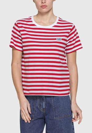 Persona che indossa una maglietta a maniche corte a righe orizzontali rosse e bianche con un piccolo logo sul petto e pantaloni di jeans blu.