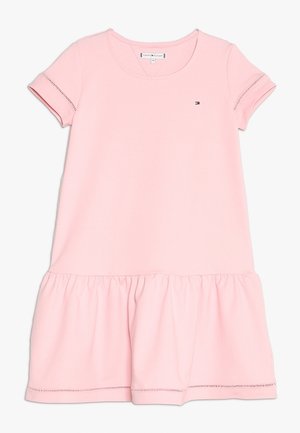 Rosa kortärmad klänning, tillverkad av mjuk bomull, har en utsvängd volangnederkant och en liten logotyp på bröstet. Rundad halsdesign.