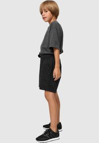 T-shirt gris à manches courtes, shorts noirs avec une taille élastique et des poches, et baskets noires avec des accents blancs.