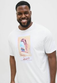 Hvid bomulds t-shirt med et farverigt grafisk design af et vindue med blomster, samt "studio" tekst nederst i rødt.