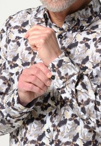 Langsleeve shirt in een bloemmotief met tinten zwart, grijs en beige. Voorzien van zwarte knopen en een conventionele kraag.