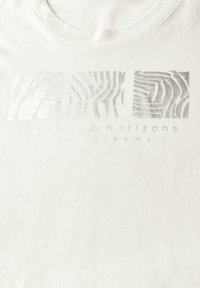 T-shirt en coton blanc avec impression en feuille d'argent présentant des motifs abstraits et le texte "horizons en expansion rêves vifs." Design col rond.