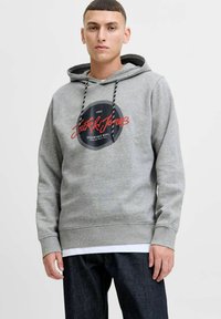 Gray hoodie with a black round logo featuring "Jack & Jones" in red. It has a drawstring closure and is paired with dark jeans.