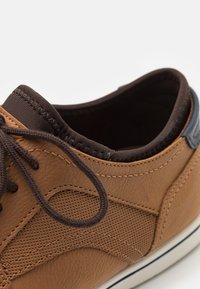 Pantof brown din piele cu panouri texturate, sireturi maro închis, guler căptușit și un accent albastru aproape de călcâi. Talpă din cauciuc alb.