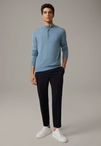 Pullover azzurro chiaro a maniche lunghe con colletto alto, abbinato a pantaloni blu scuro e sneaker bianchi, con un taglio casual e una superficie liscia.