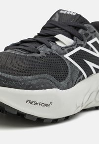 Scarpa sportiva nera con parte superiore in rete e suola in gomma, con dettagli bianchi e il marchio "FRESH FOAM" sul lato. Elementi di design testurizzati visibili.