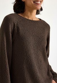 Maglione marrone con texture, collo rotondo e maniche lunghe. Il tessuto presenta un sottile motivo intrecciato e una vestibilità rilassata.