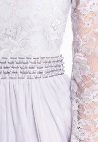 Krajková šaty s dlouhými průhlednými rukávy, fialová látka, zdobený pas perlami a stříbrnými akcenty, s texturovanou tylovou sukni.