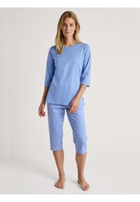Blauw pyjamapak met een effen top met driekwart mouwen en een patroon van capri-broekjes in lichtblauw met witte hartontwerpen.