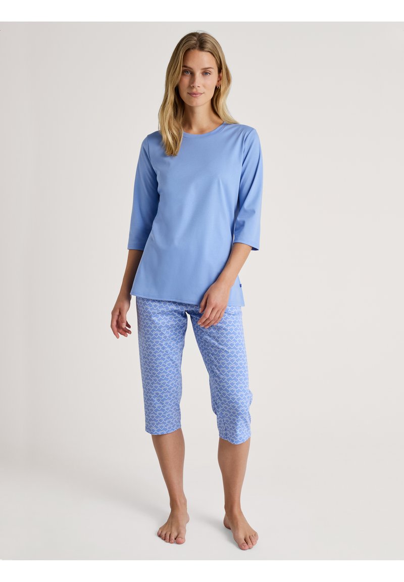 Blauw pyjamapak met een effen top met driekwart mouwen en een patroon van capri-broekjes in lichtblauw met witte hartontwerpen.