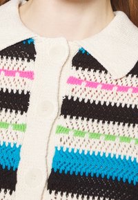 Stickad cardigan med krage, i en krämfärgad bas med randiga mönster i svart, rosa, grön och blå. Sex knappar som detaljer.